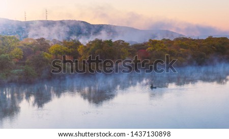 Water evapoation on the river at dawn and lonely fisher on a boat at autumn season