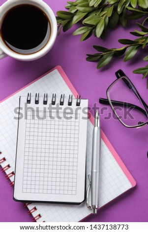 a few notebooks and glasses, a cup of coffee and flowers on a bright purple background. top view. office tools
