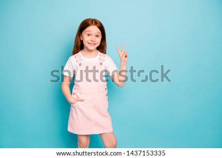 Portrait of lovely cute kid make v-signs look stand hands palms pockets isolated over blue background