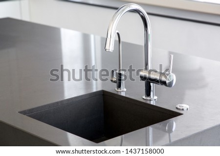 kitchen sink of dark gray stone with chrome faucet in a clean kitchen with a glossy work surface, close up faucet sink. Royalty-Free Stock Photo #1437158000