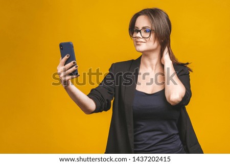 Closeup of beautiful playful business woman making selfie photo on isolated yellow background and looking at camera.