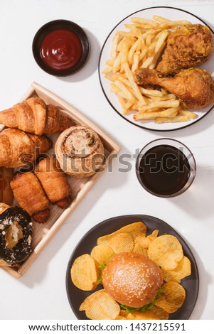 Freshly baked buns, big hamburger, fried crispy chicken and french fries on white table - Unhealthy food concept