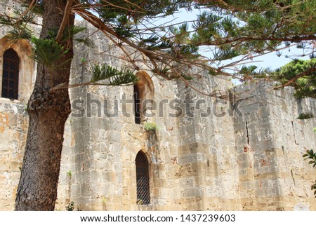 
The walls of the ancient museum in the foliage of trees. The Crusader-era cathedral of Our Lady of Tortosa. syria.  Catholic cathedral in the city of Tartus Royalty-Free Stock Photo #1437239603