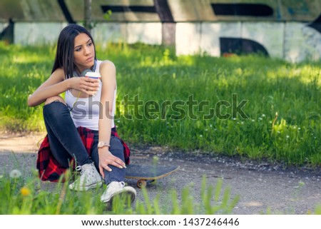 Urban girl sitting on skateboard on street. Outdoors, urban lifestyle.
