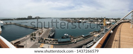 Panoramic picture of harbor in Miami Florida from aboard Norwegien Sky. Small people are visible, along with blue water and a grey blue sky.