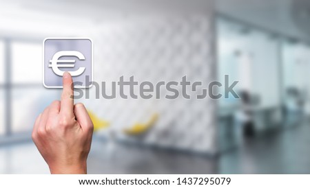 Hand with index finger over white stylized euro symbol with blurry modern detailed room in background