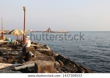
embankment of the city of Tartus, Syria. A Muslim woman in a white headscarf is sitting on the background of the sea. open umbrella Royalty-Free Stock Photo #1437308933
