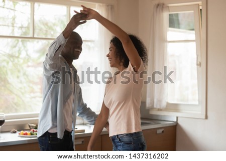African guy mixed race girl holds hands moving at home, overjoyed couple in love wife and husband standing in the modern cozy kitchen dancing feels happy, having romantic date spend free time together
