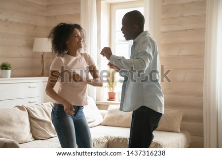 Happy romantic african couple having fun in new home first apartments, wife and husband dancing enjoy active weekend, funny american family feel excited spends time together in cozy modern living room