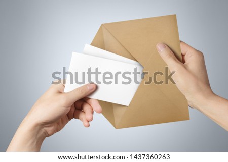 Hands pulling two blank sheets of paper (tickets, flyers, invitations, coupons, banknotes, etc.) out a brown envelope on gray background