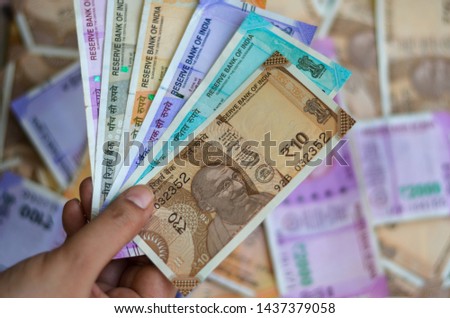 Closeup of brand new colorful Indian currency bank notes of 10, 50, 100, 200, 500 & pink 2000 rupees bundle issued and in circulation after demonetisation held with hand with many notes in background Royalty-Free Stock Photo #1437379058
