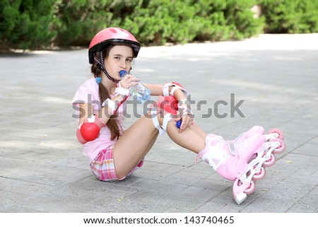 Little girl in roller skates drinking water at  park