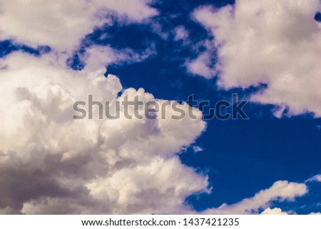 Large fluffy white clouds glow over the blue day sky