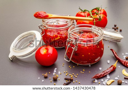 Tomato confiture, jam, chutney, sauce in glass jar. Homemade preservation concept. Fresh tomatoes, dried chili, spices, mustard beans, sea salt. On a stone background Royalty-Free Stock Photo #1437430478