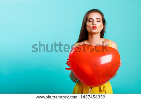 beauty portrait model brunette girl in studio on blue background posing in yellow fashionable dress with red balloons in their hands. - Image          