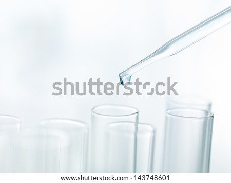 A macro of a pipette adding a drop of fluid  to one of several cylindrical phials on a light background
