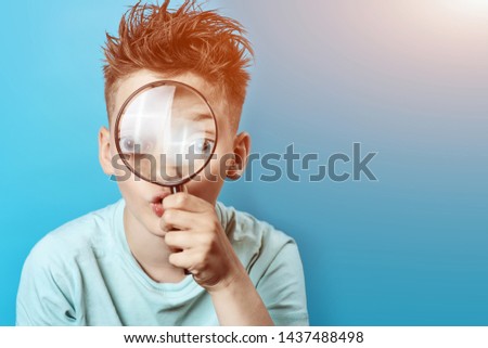 a boy in a light t-shirt looking into a large magnifying glass