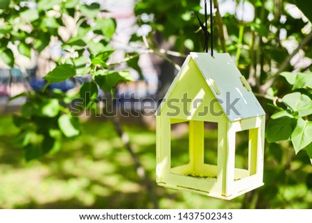 Yellow bird house hanging from the tree and surrounded by lush foliage. Nest box on a green background with copy space