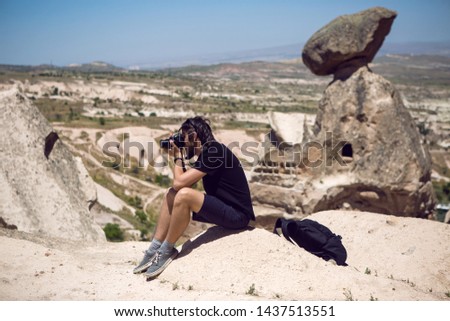 man in a black t-shirt sitting on a rock and taking pictures of the views