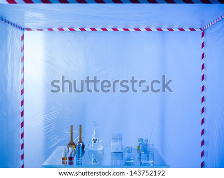 different glass containers filled with differently colored liquids on a glass table in a containment tent, lit by a blue light