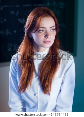close-up of beautiful redhead female assistant with a blackboard with formulas on background