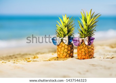 Couple of attractive pineapples in stylish colored sunglasses on the sand against turquoise sea. Tropical summer vacation concept. Sunny day on the beach of tropical island. Honeymoon. Family holiday