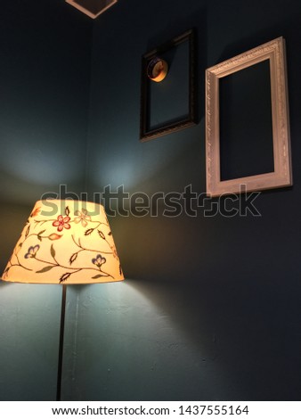 A lit flower lamp in a dark room with abstract empty frames on the wall and an ashtray in one of them