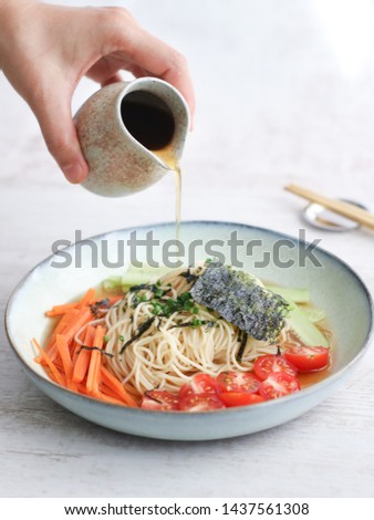 Japanese Zaru cold noodles made with spaghetti angel hair, hand pouring soy sauce for dipping, it's a traditional chill dish for summer served with mixed colorful vegetables and seaweed 