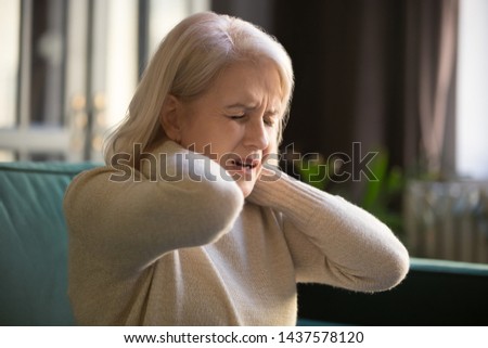 Tired upset old senior woman feeling stiff sore neck pain concept rubbing massaging muscles suffer from fibromyalgia ache, mature middle aged grandma having pinched nerve problem stretching at home Royalty-Free Stock Photo #1437578120