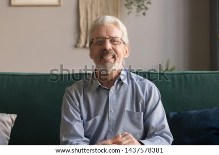 Happy senior retired man blogger looking at camera recording vlog, smiling old elder grandfather talking to webcam make distance online call or video chat sit on sofa at home, webcamera view portrait Royalty-Free Stock Photo #1437578381