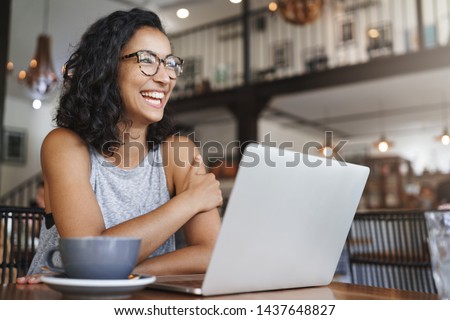 Side-shot enthusiastic happy carefree female student prepare freelance project working laptop sitting cafe laughing joyfully contemplate outside window wear glasses enjoy cappuccino Royalty-Free Stock Photo #1437648827
