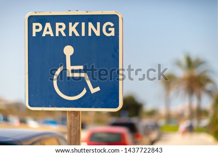 A blue and white sign in front of a hospital that allows disabled drivers to park their car here. The place is in Spain with sunshine and blue sky.