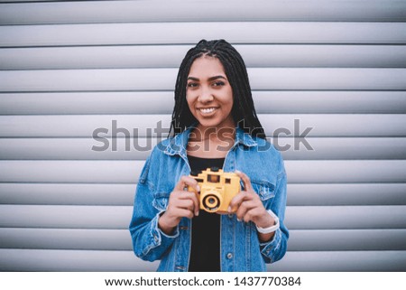 Half length portrait of happy female amateur photographer holding old fashioned technology in hands and looking at camera near promotional background, successful woman with vintage equipment