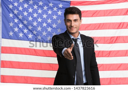 Smiling Caucasian businessman in black suit standing and crossed his arms in front of an American flag background.