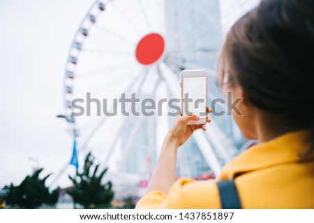 Back view of generation female influencer taking pictures of Chinese ferris in Hong Kong using mock up cellphone gadget with blank screen area for text advertising, blogger photographing wheel