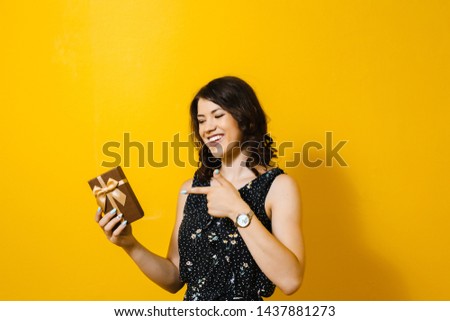 The image of a happy smiling girl opening a gift box and showing isolated gestures over a yellow background