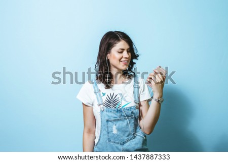 Portrait of happy woman wearing earphones singing isolated over blue background