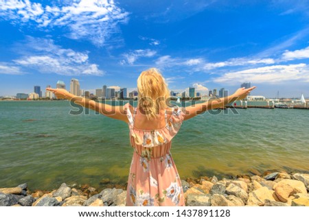Blonde lady enjoying at San Diego Downtown skyline with skyscrapers in California, USA from Coronado Island. Tourist woman in summer american holidays. Waterfront and urban cityscape in San Diego Bay.