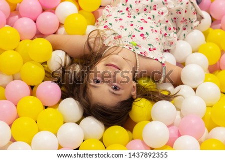 Beautiful little girl in the playground full of colorful balls, with copy space 