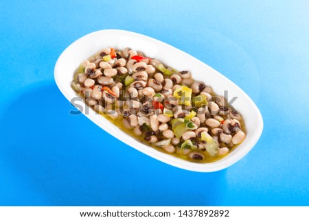Delicious black eyed pea salad with olive oil and lemon at white plate isolated on blue background.