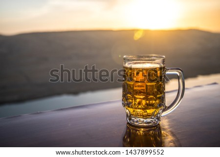Glass of beer on a beach at sunset. Cooling summer drink concept. Close Up of A Glass of Draught Beer with the Bokeh of Sunlight Background, Soft Focus