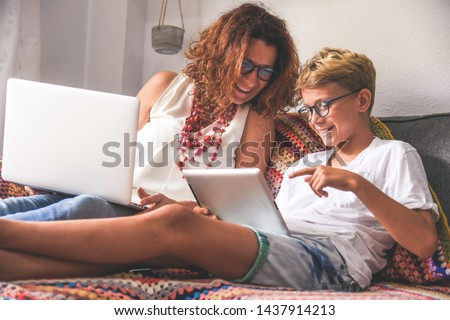 Beautiful teen reading new trend stories online on tablet with mum. Technology addicted young boy watching social video at home with his mother. Child and mommy communicate and plays with tech device. Royalty-Free Stock Photo #1437914213