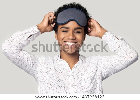 Happy african American millennial woman isolated on grey studio background wearing sleepwear accessory on head, smiling black biracial girl with gray sleeping mask look at camera feel refreshed