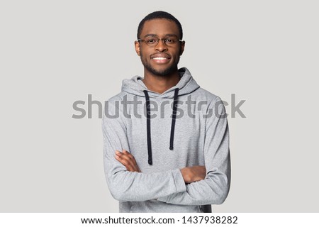 Portrait of smiling african American man in glasses and sportswear isolated on grey studio background pose for picture, happy black male in eyewear and hoodie stand with arms crossed look at camera Royalty-Free Stock Photo #1437938282