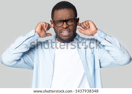 Annoyed african American millennial man in glasses close plug ears avoid unpleasant disturbing sound, unhappy black male in spectacles isolated on grey studio background bothered by bad loud noise Royalty-Free Stock Photo #1437938348
