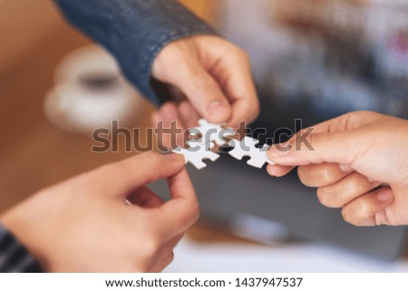 Closeup image of many people hands holding and putting a piece of white jigsaw puzzle together