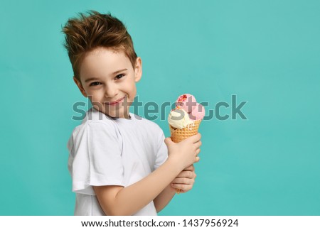 Baby boy kid hold three scoops of strawberry and vanilla ice cream in waffles cone on blue mint background with free text copy space