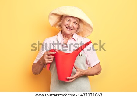 beautiful happy girl in grey apron and yellow hat holding watering can, isolated on yellow background. close up photo.gardern concept. lifestyle, free time, spare time, studio shot