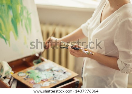 woman holding many brushes while painting. close up side view cropped photo