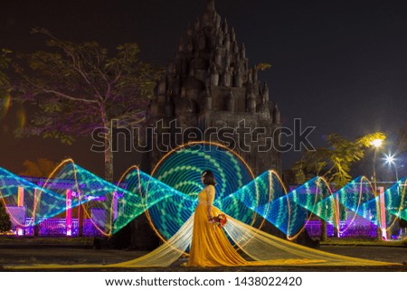 Beautiful Indonesian females wearing yellow long dress was standing decorated with a green light painting as a backdrop on the site area of ​​a night tour